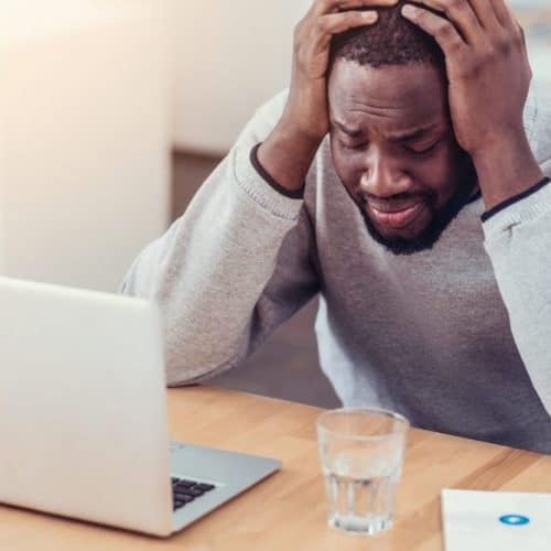 Cannot stand it anymore. Emotionally exhausted young man in casual getting emotional and pressing his head in hands while sitting at a laptop and struggling with a serious project at work.